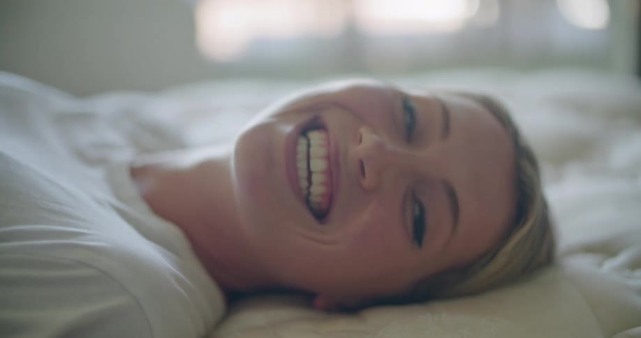A woman lays in bed and covers her mouth while laughing