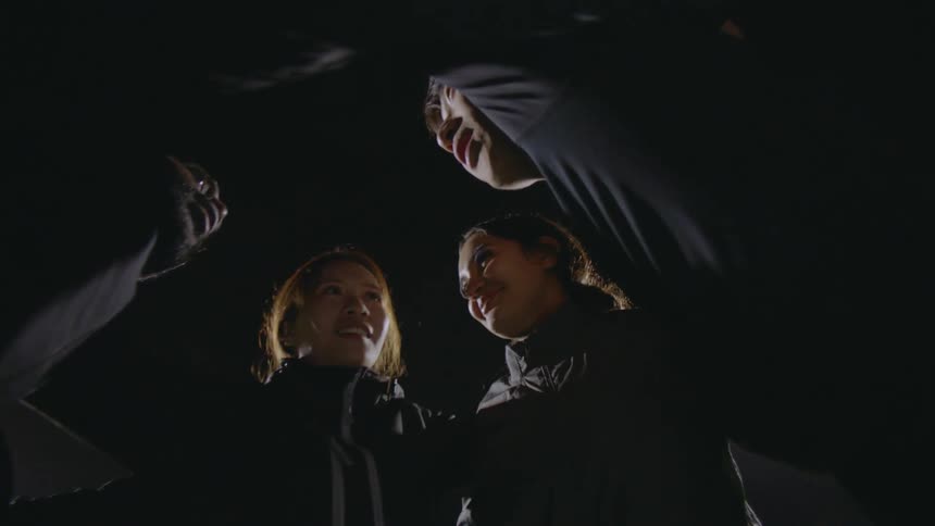 Friends smile at each other standing a group hug outdoors at night