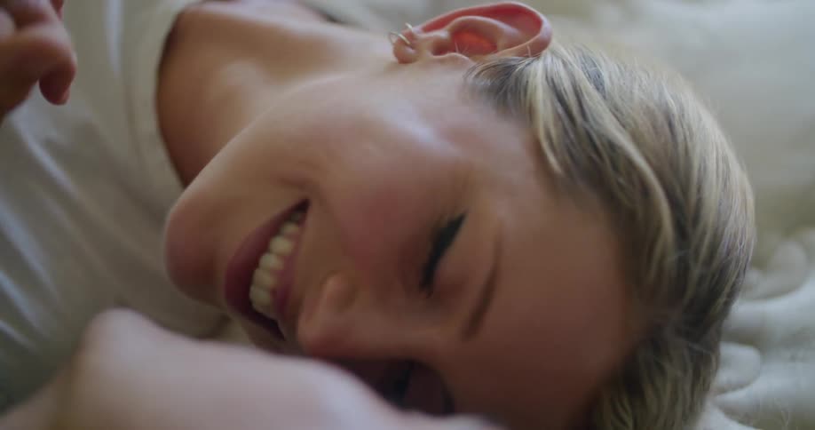 A woman smiles as she leans forward to kiss her husband as they lie side by side on a mattress