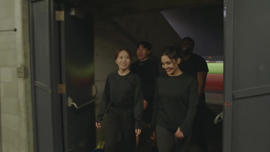 A group of people chat and high five one another while walking off on an athletics track and into a building