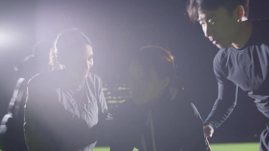 Young tired woman is greeted and cheered up by her friends on a field near the city at night