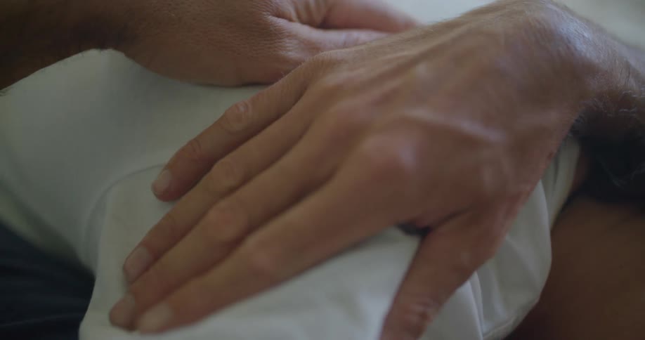 Man rubs the back of a sleeping woman while resting in bed