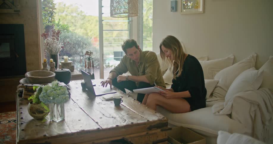 Man and woman work with computer and notepad in living room with glass doors showing a forest in background