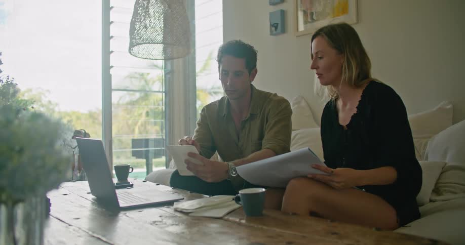 A woman sketches in a notebook as she and a man look at a laptop together
