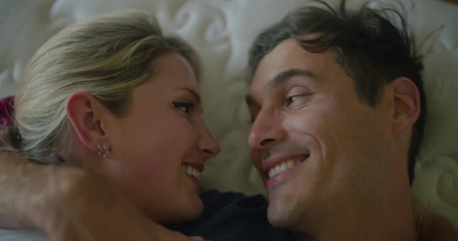 A man pulls his girlfriend in close and kisses her as they lie in bed