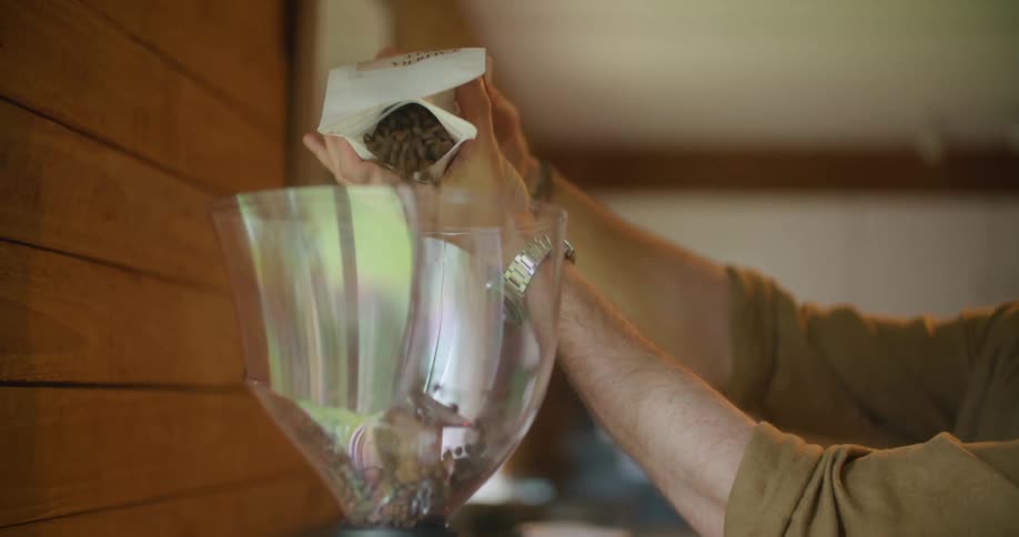 A man in a coffee shop pours coffee beans in to a machine