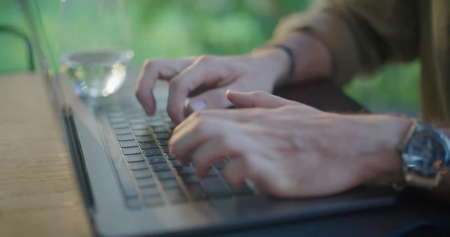 Man with green shirt and wristwatch types on laptop keyboard in green garden