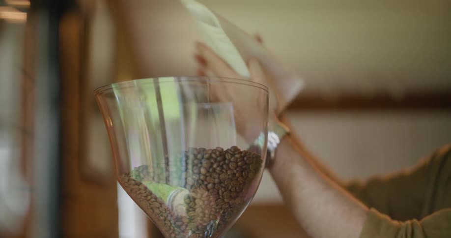 Man pours coffee beans into glass bin then puts the lid on it