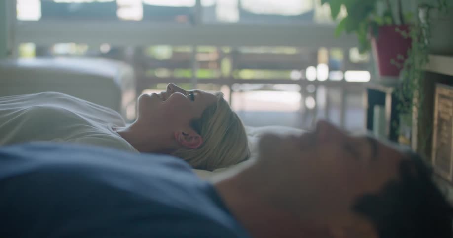 Couple lies down on bed and looks at each other
