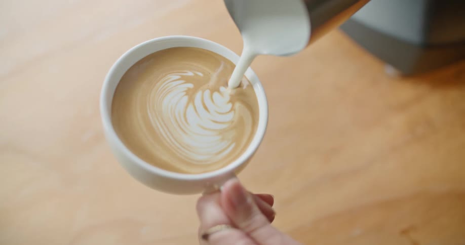A woman preparing a latte in a white ceramic mug