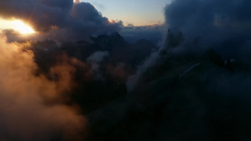 The sun is shining brightly through the clouds with mountains in the distance