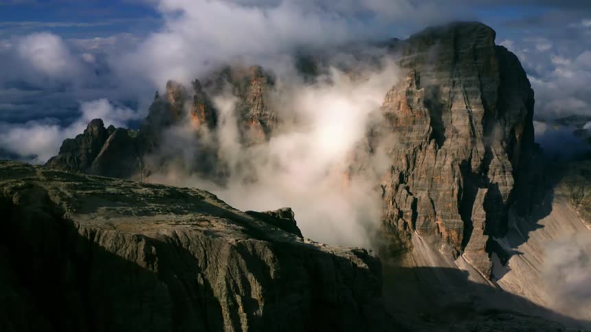 A rock mountain peak shrouded in fog during the day