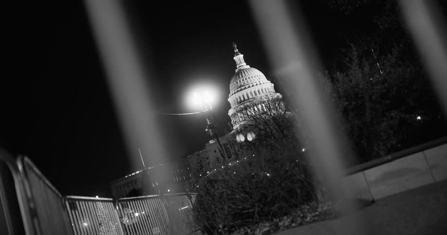 The capitol building at night with the lights on seen through the fence