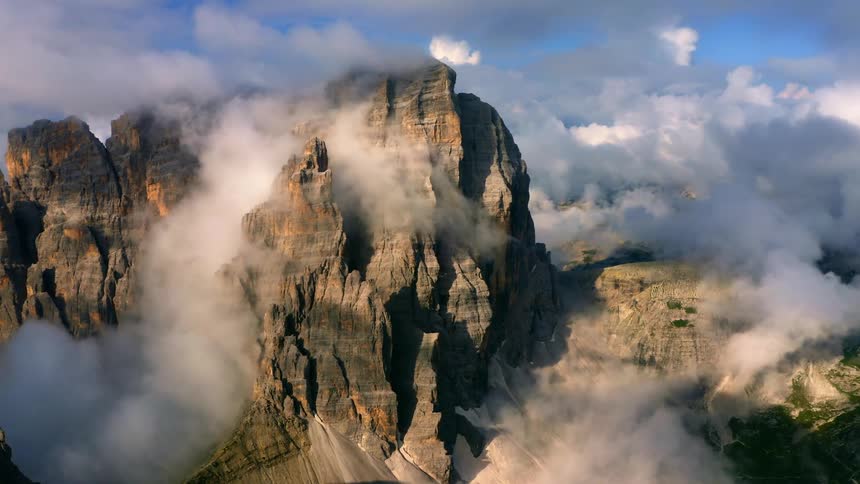 A mountain cliff surrounded by clouds and mist during the day