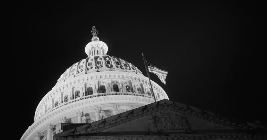 American flag flying near the dome of the capitol building at night