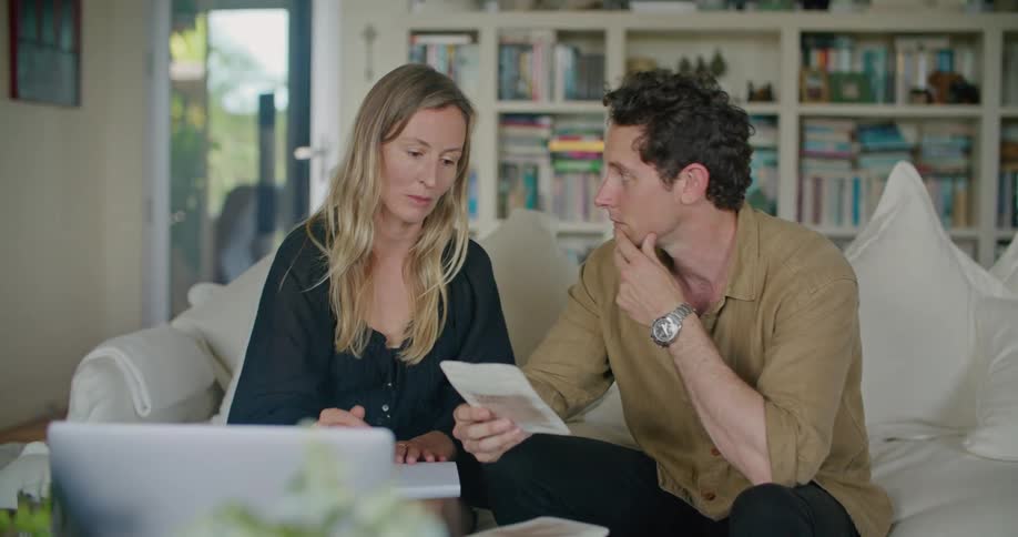 Two people sit on sofa near laptop discussing label on packaging