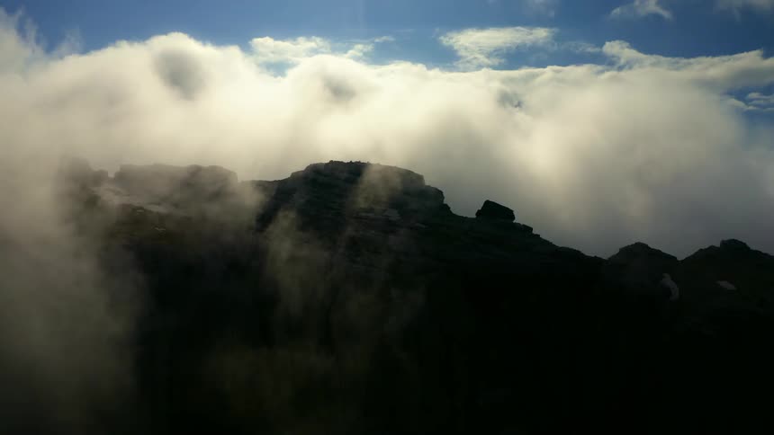 Clouds move over a mountain ridge high in the sky