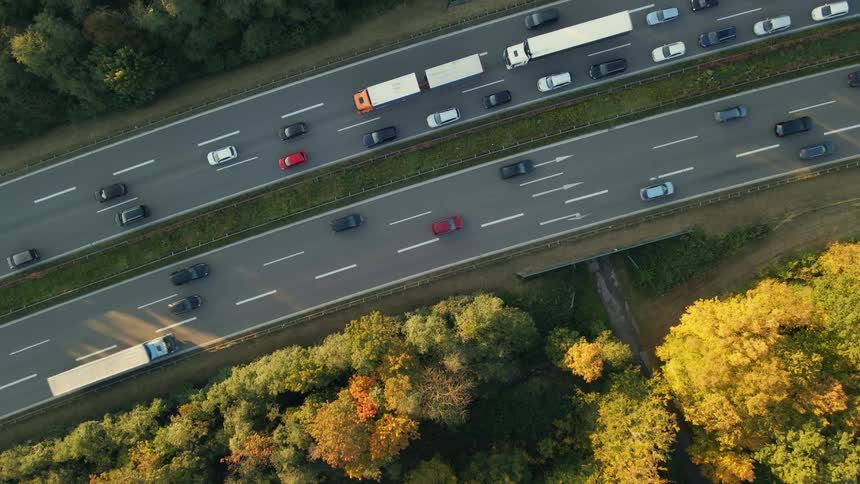 Cars and trucks commuting on a freeway surrounded by autumn trees in the daytime
