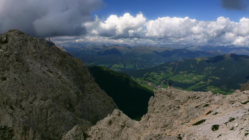 Jagged mountain ridge reveals a green valley and village beneath a blue sky