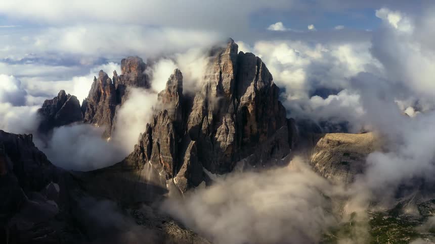 Aerial view of clouds hanging over the jagged slopes and cliffs of a tall mountain