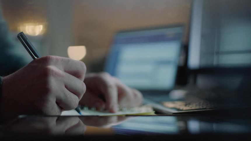 A man writes in a notebook at his desk
