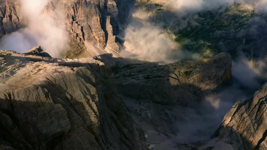 An aerial view of a canyon with grass areas and patches of dense fog in the daytime