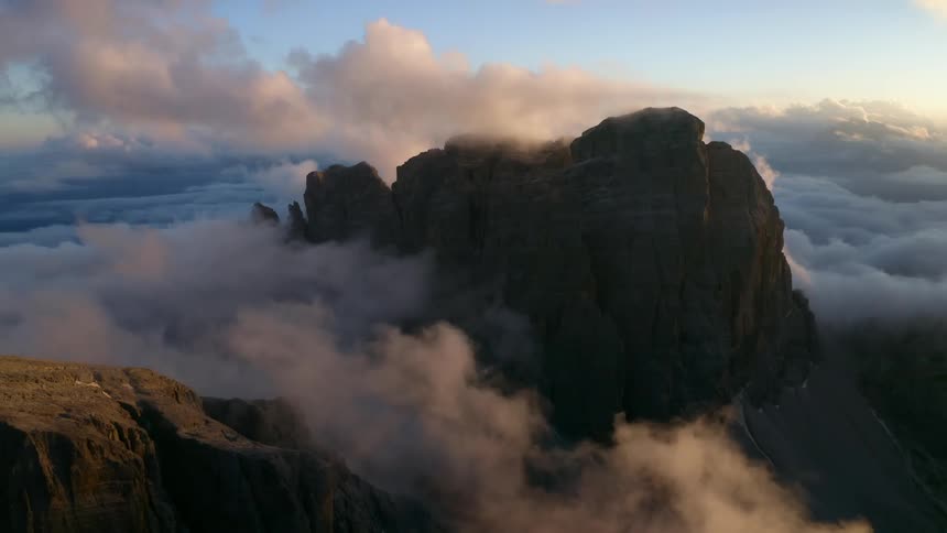 Clouds floating around a rocky mountain range during sunrise in nature