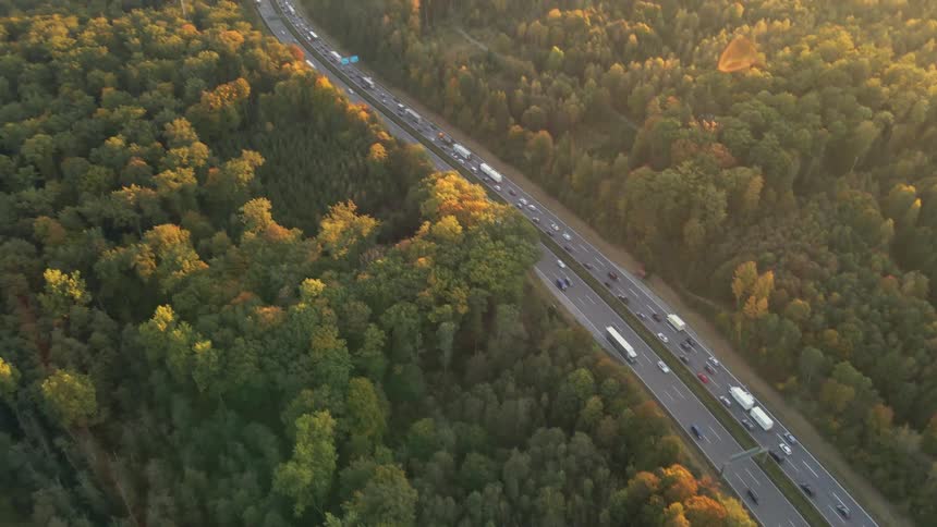 Aerial view of traffic on a busy highway and trees along the side of the road in fall colors as the sun shines brightly on the horizon