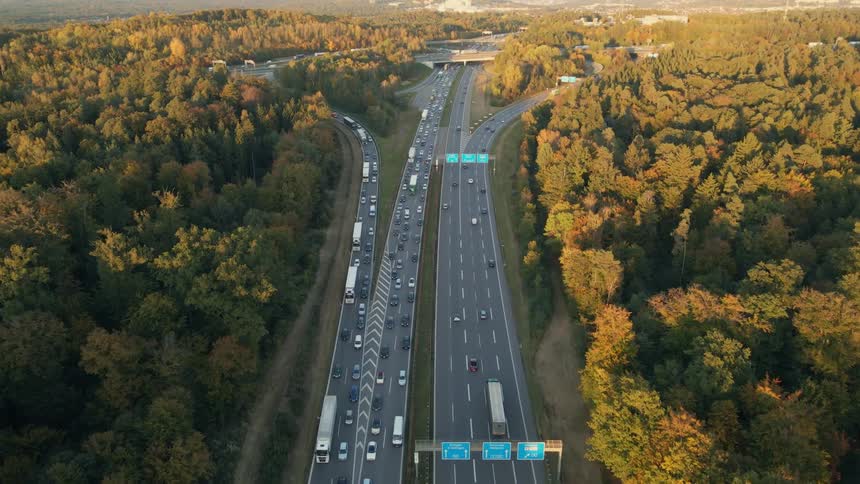 Traffic jams frontage road as highway flows to and from forest with fall foliage