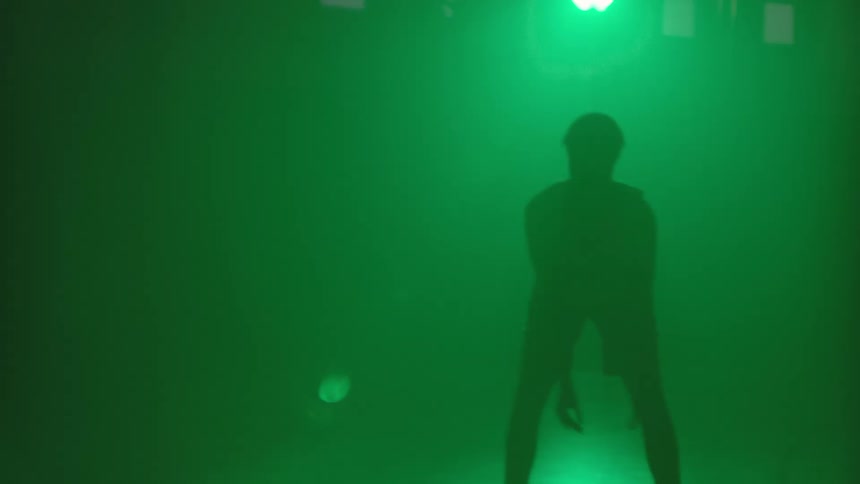 Basketball player dribbles ball silhouetted by green light