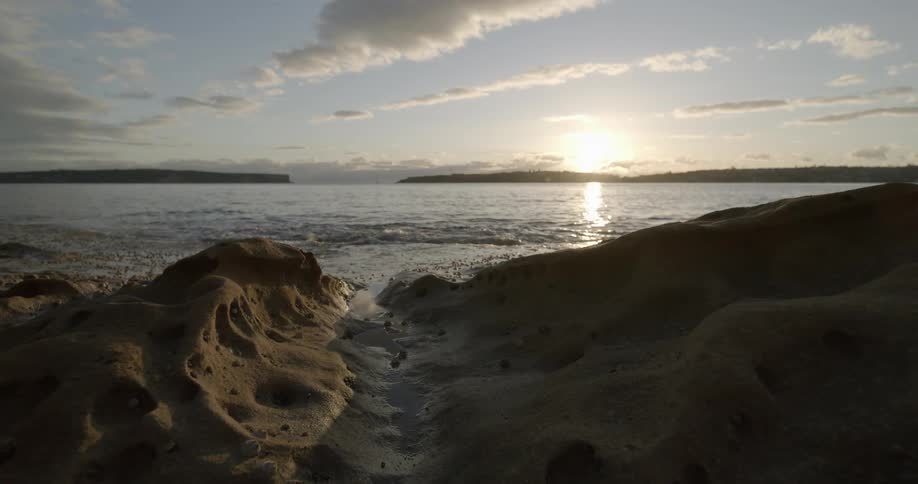 Waves roll in over the shore as the sun shines brightly on the horizon