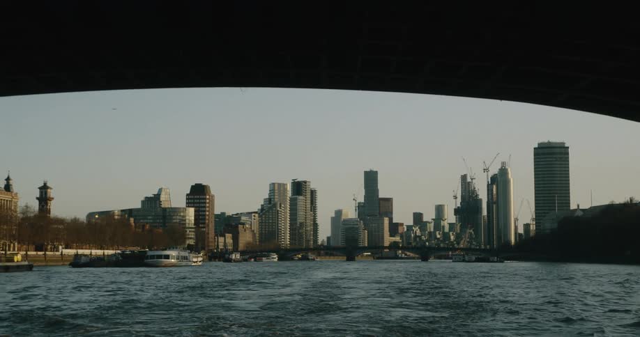 Pedestrians walking over a bridge over a river next to the city skyline at evening