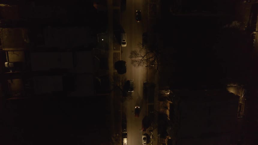 Cars drive along street past apartment buildings at night