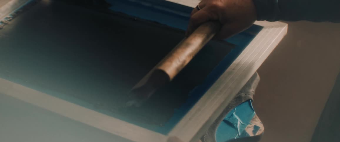 A man uses a tool to smooth a design being printed on a graphic t shirt