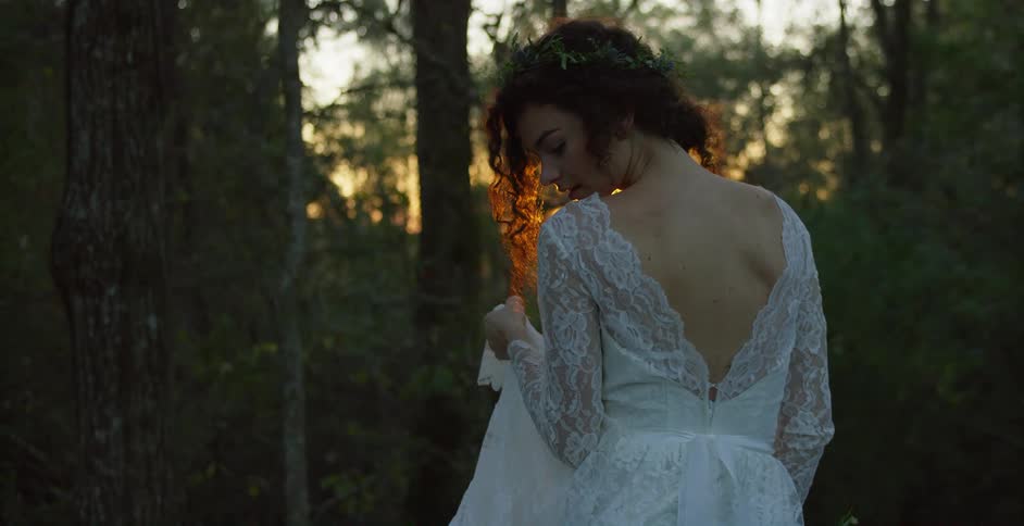 Young woman in a white wedding dress standing in the forest at sunset