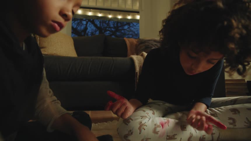 Siblings sit on sheet covered wooden floor in living room while they finger paint