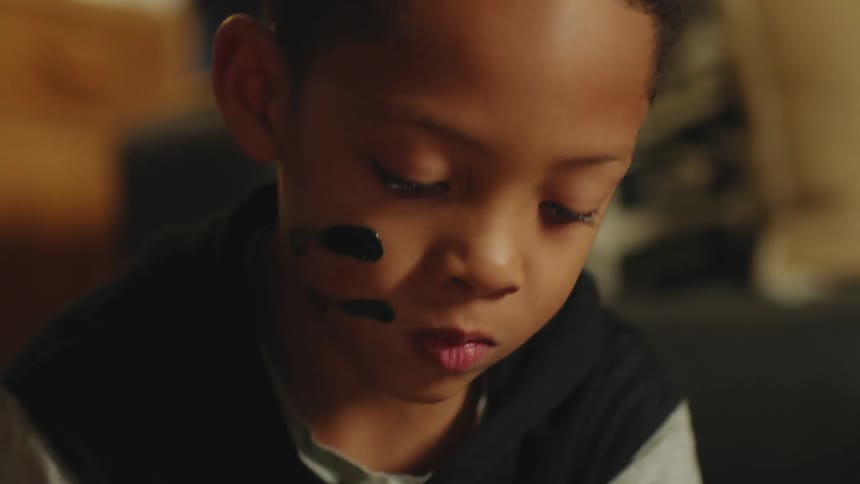 A boy uses his fingers to smear lines of paint on his face