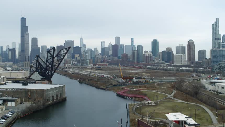River flows under bridge passing construction site and downtown skyscrapers