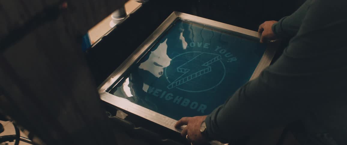 A man holds a frame down on a screen printing logo for tee shirts