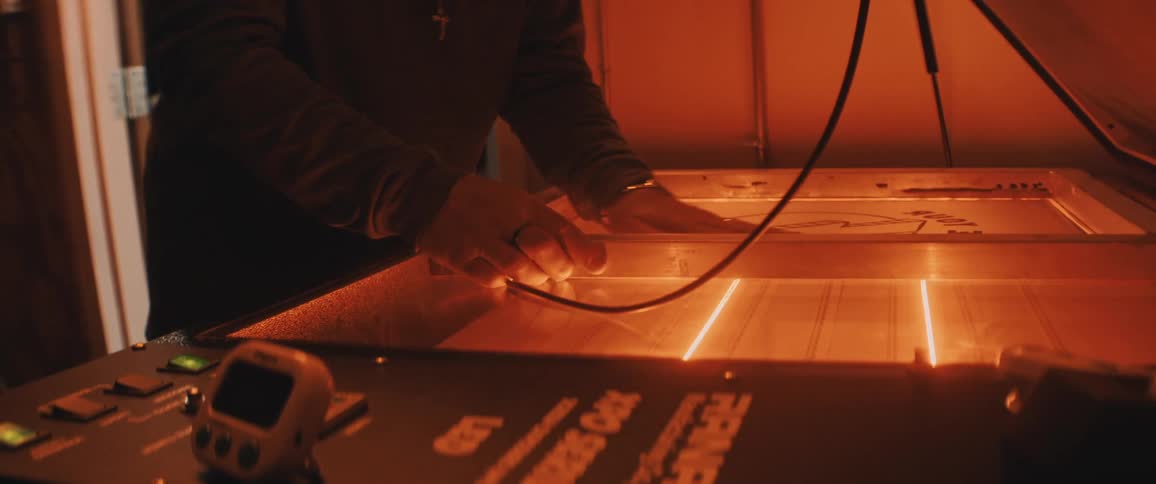 A man in a shop lies a frame on a sign in a machine and closes the lid