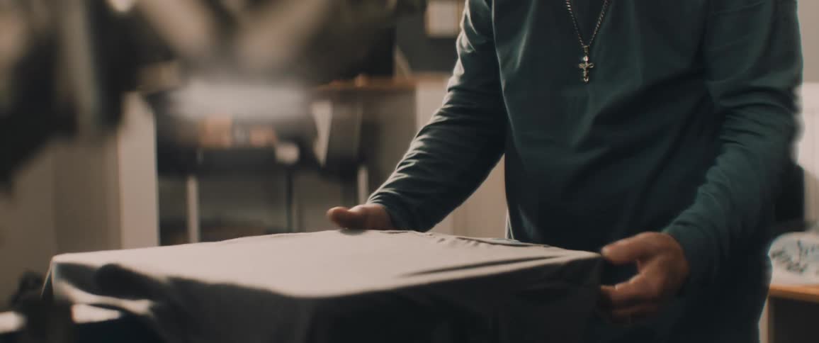 A man wearing a white bandanna is putting a shirt into a silk screen printer