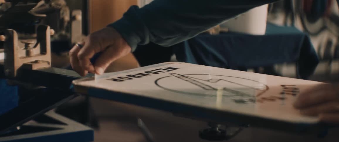 Man screen printing a sheet of clear plastic with ink over a table