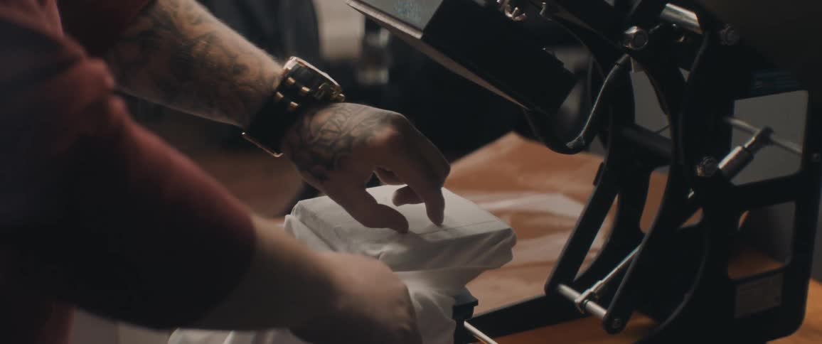 A man is working in a print shop and pressing a graphic design onto a shirt