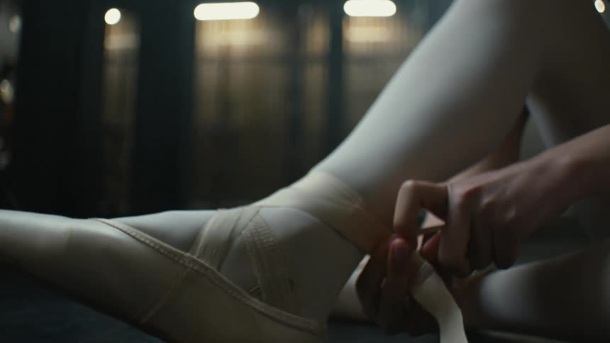 Ballerina tying up her ballet shoes while sitting on stage