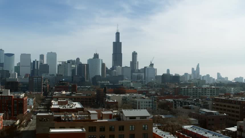 An aerial view of apartment buildings in a city with cars parked and driving down the streets with the downtown skyline in the distance