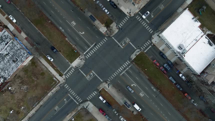 Aerial view of traffic at an intersection with buildings and parked cars along the side of the road