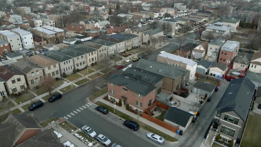 Vehicle drives down street past apartment buildings in neighborhood with city on horizon