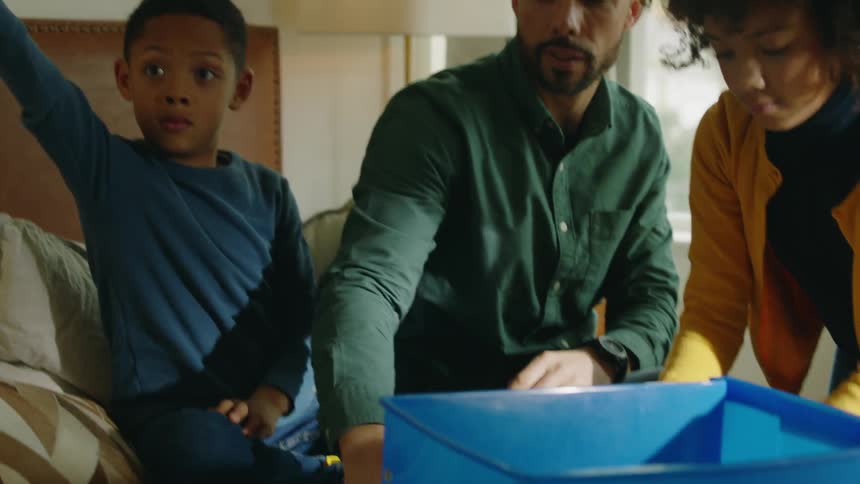 Family puts small toy pieces sitting on bed into bin