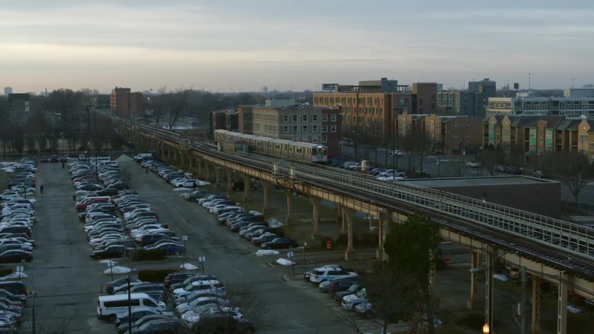 Passenger train moves along elevated track between parking lot and apartment buildings