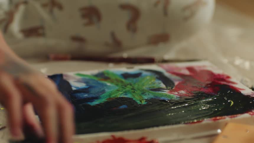 A painter smears acrylic paint on a canvas on the floor